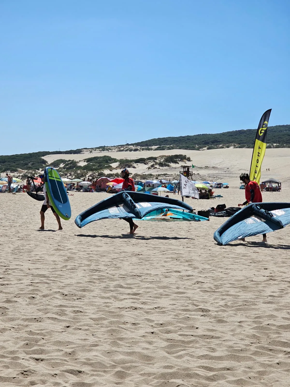 Grupo caminando por la playa con alas de wingfoil en Tarifa